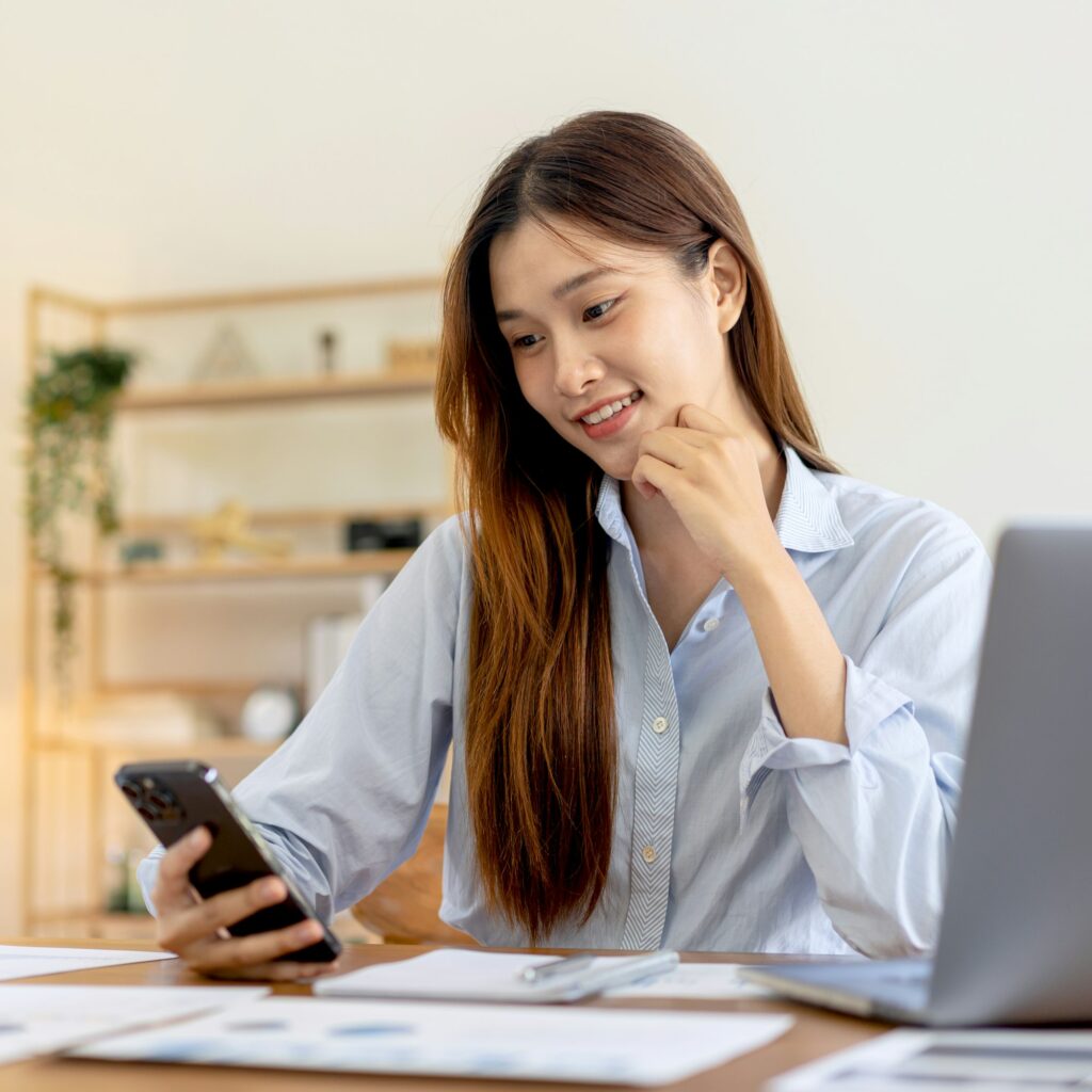 Female freelance is reading business data on smartphone and while using laptop to working on table