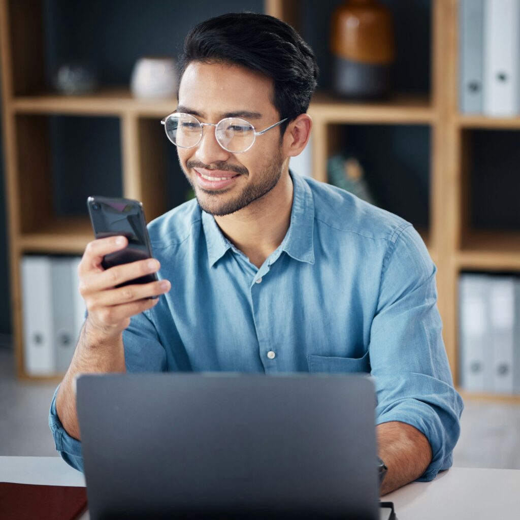 Happy asian man, phone and laptop for social media, communication or networking at office desk. Mal